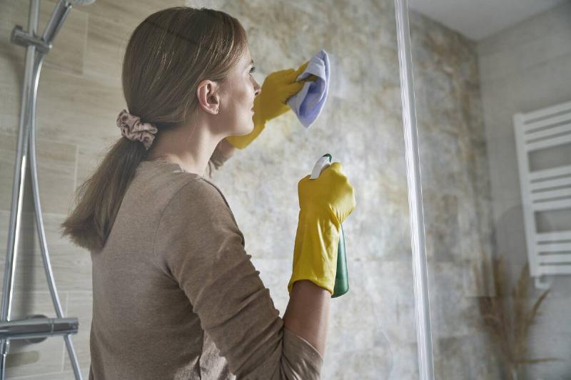 Young woman cleaning shower glass.