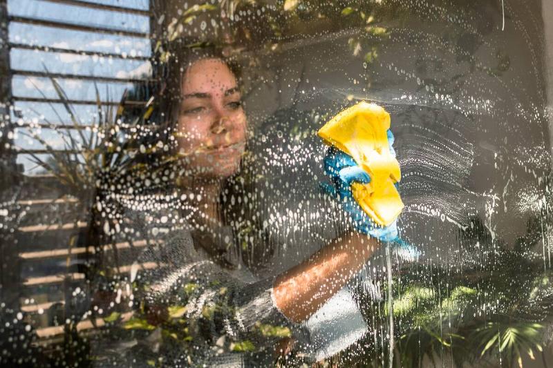 A young female cleaning a window with a wiper and sponge. 