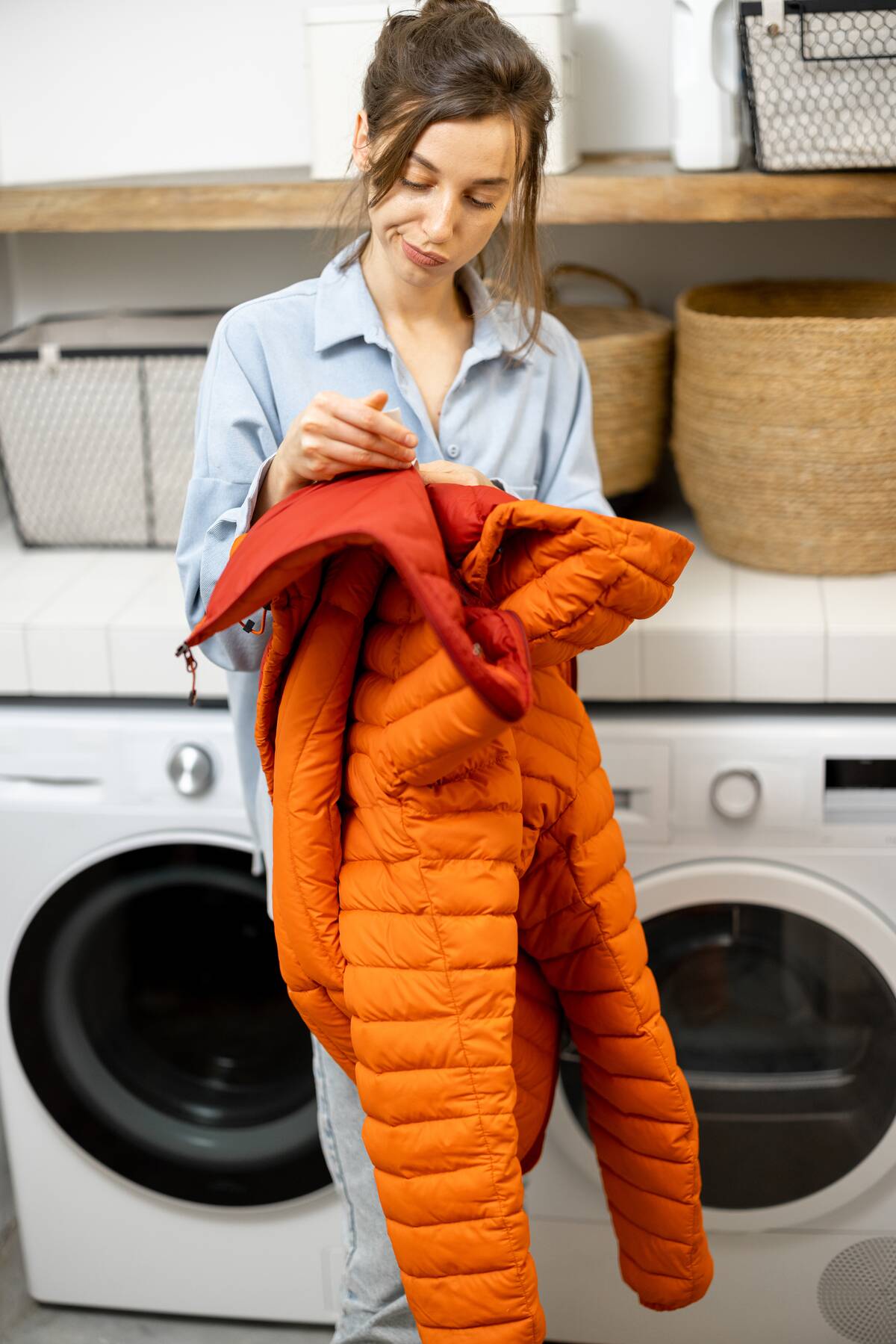 Woman holding orange winter jacket in laundry room. 