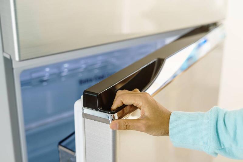 A hand opening a fridge door and showing the seal on the door. 