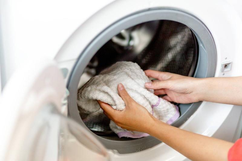 Hands putting cloths into a washing machine. 