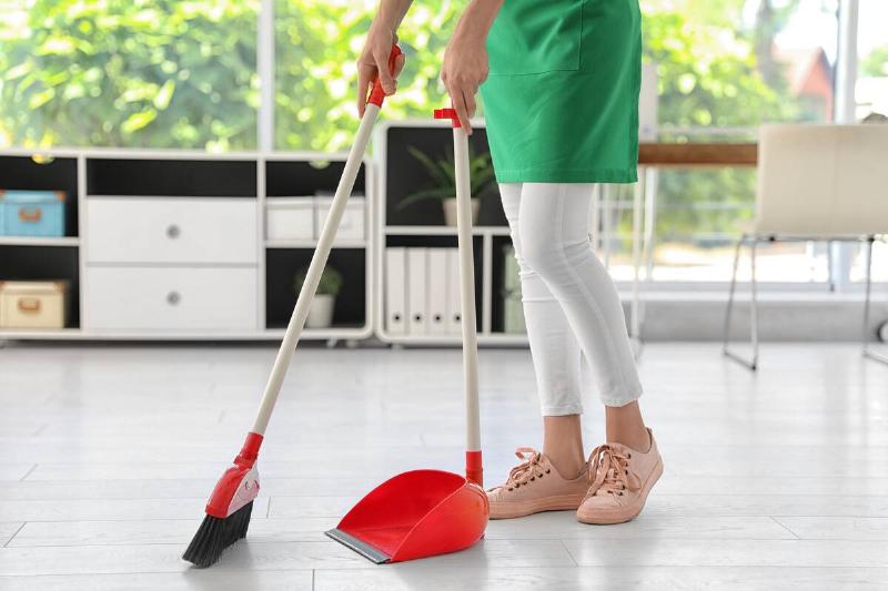 Young woman sweeping with broom and dustpan.
