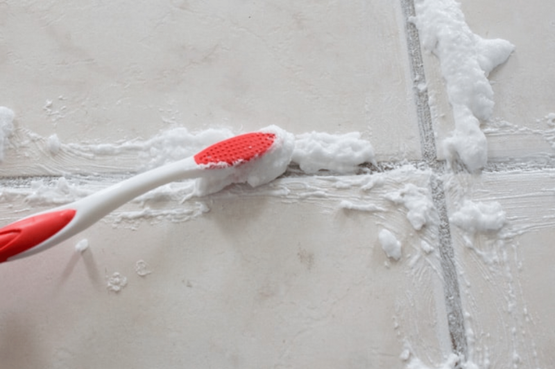 A toothbrush scrubbing hydrogen peroxide paste into grout.