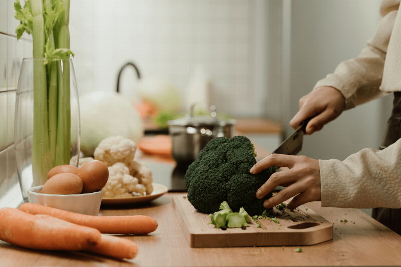 A person cutting vegetables on a wooden cutting board. 