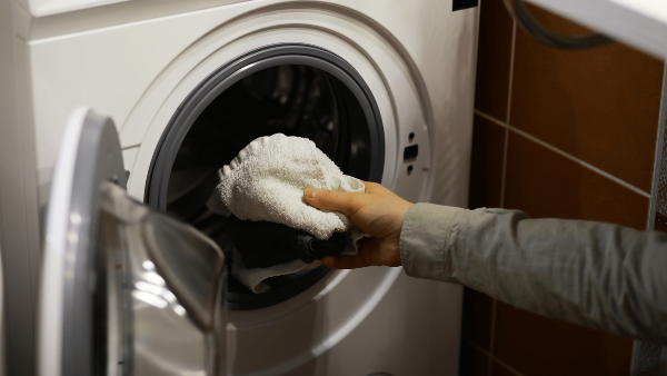 Hands putting laundry in a washing machine.