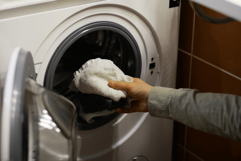 Hands putting laundry in a washing machine.