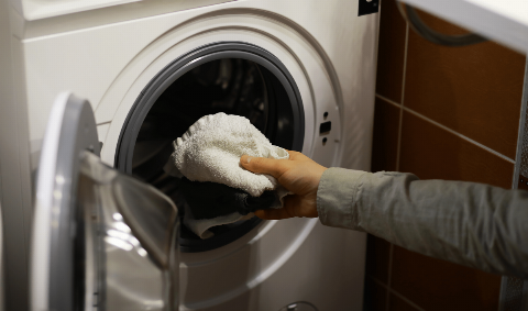 Hands putting laundry in a washing machine.
