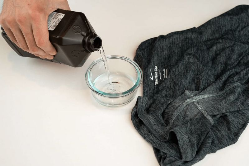 Hydrogen peroxide being poured into a glass dish and a black shirt. 