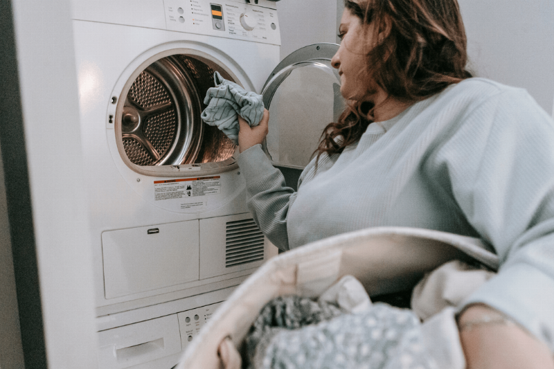 Woman putting clothes in dryer. 