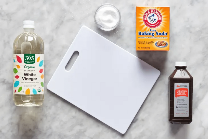 A white plastic cutting board with baking soda, hydrogen peroxide, and white vinegar. 