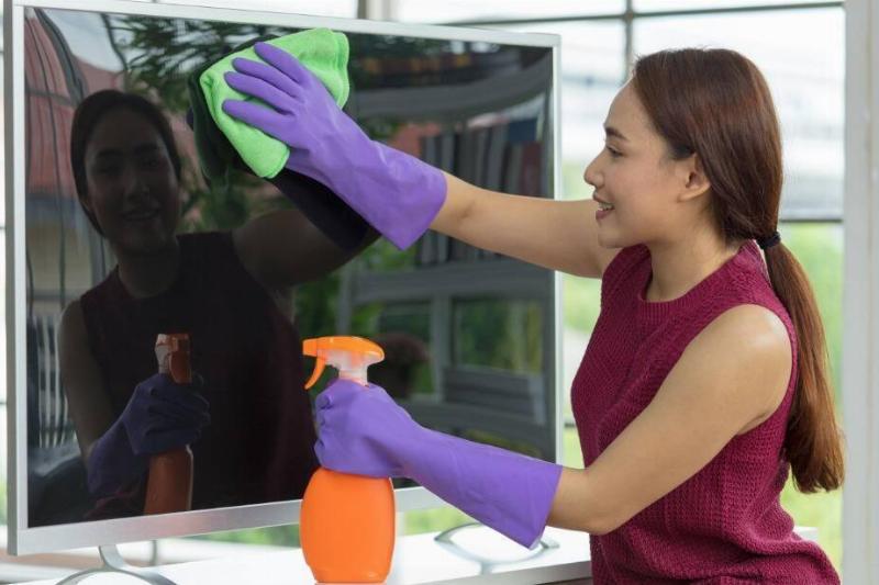 A woman wiping a TV with a spray bottle. 
