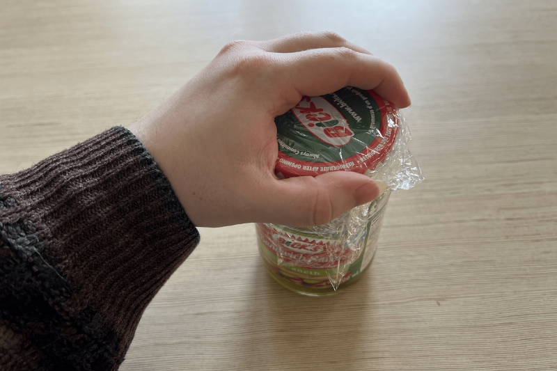 A hand opening a jar with plastic wrap on it. 