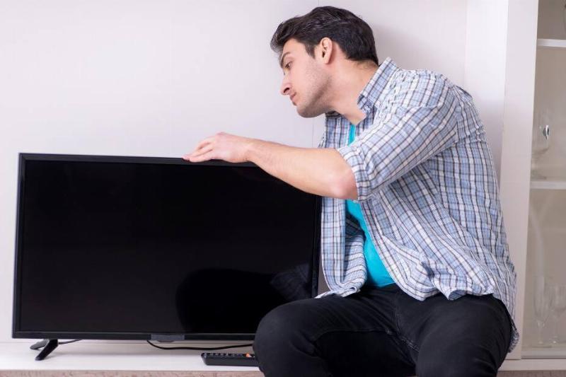 A man looking behind a TV. 