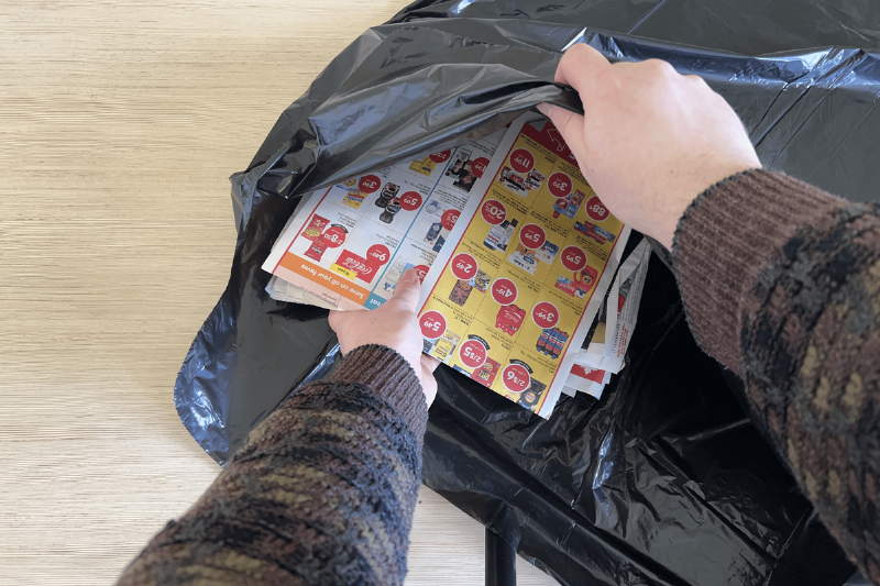 Hands putting flyers in a garbage bag. 