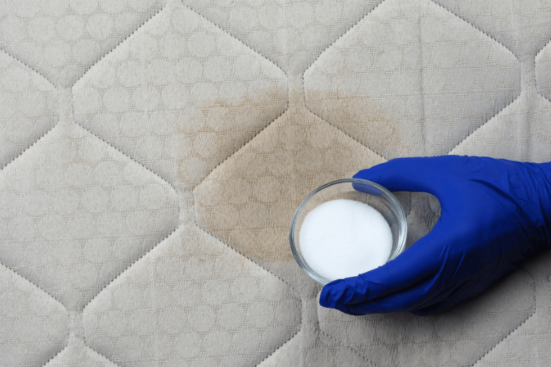A hand holding baking soda on a mattress. 