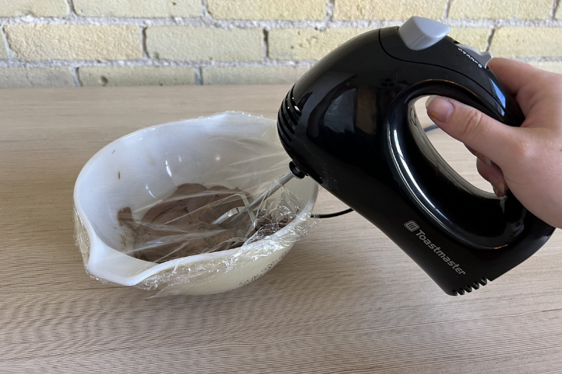 A mixer in a bowl with plastic wrap. 