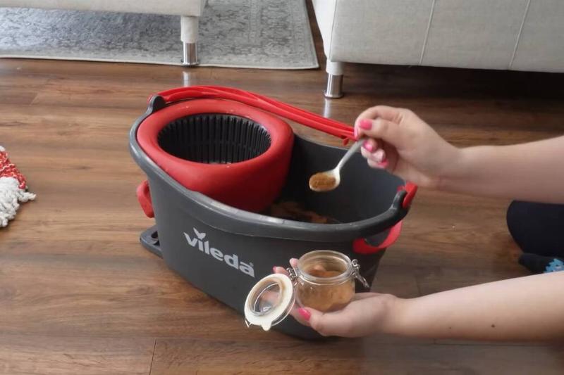 A person putting a spoon of cinnamon in a mop bucket. 