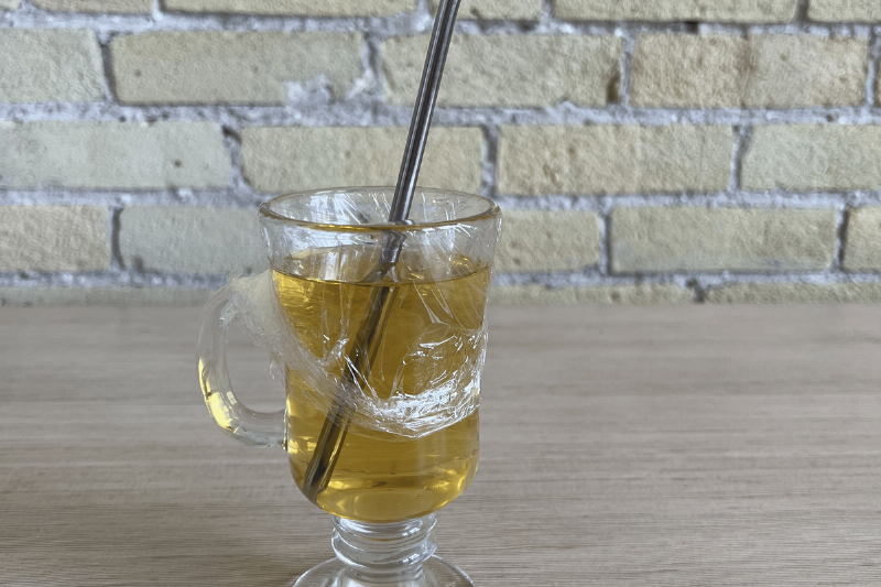 A drink in a glass with plastic wrap over the top.