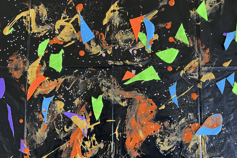 Glitter, paint, and other craft supplies on a black garbage bag. 