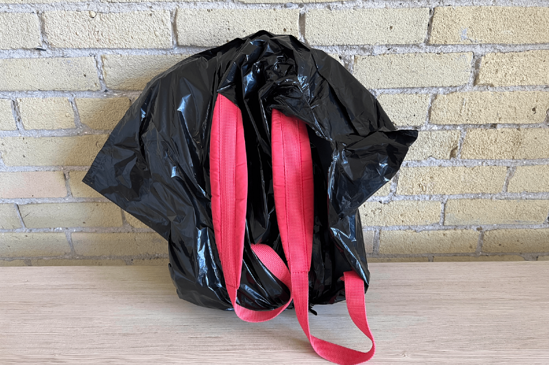 A backpack covered by a garbage bag. 