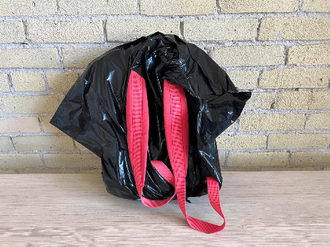 A backpack covered by a garbage bag. 