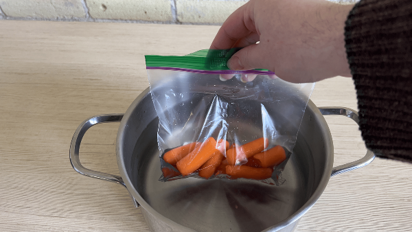 A hand putting baby carrots in boiling water. 