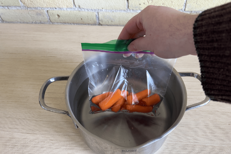 A hand putting baby carrots in boiling water. 