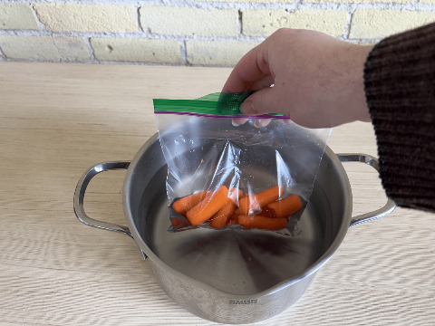 A hand putting baby carrots in boiling water. 