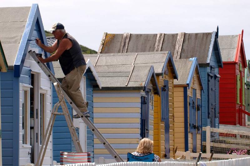 A man on a ladder painting the roof of a house. 