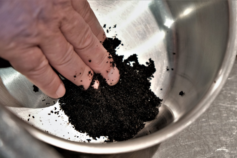 A hand holding coffee grounds in a stainless steel bowl. 