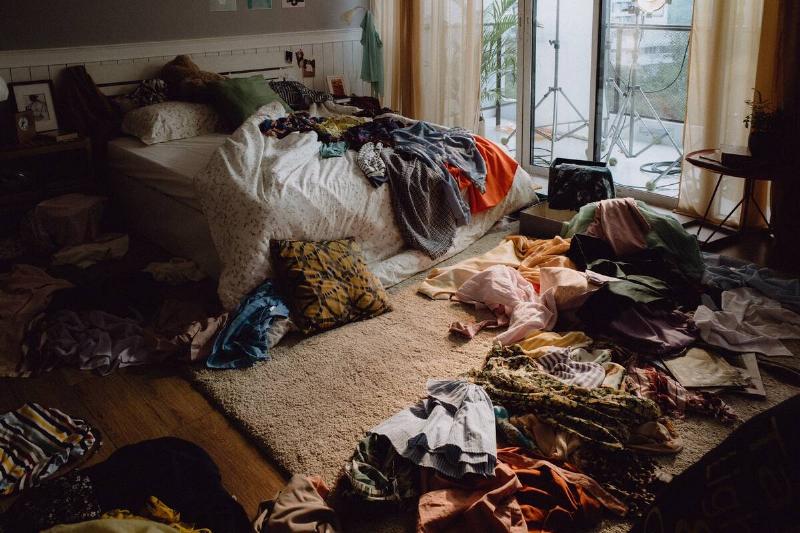 The inside view of a messy bedroom with clothes everywhere. 