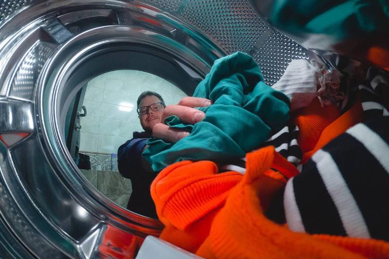 Hands putting clothes in a dryer. 