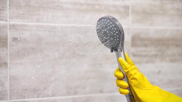 Hand in yellow glove holding shower head. 