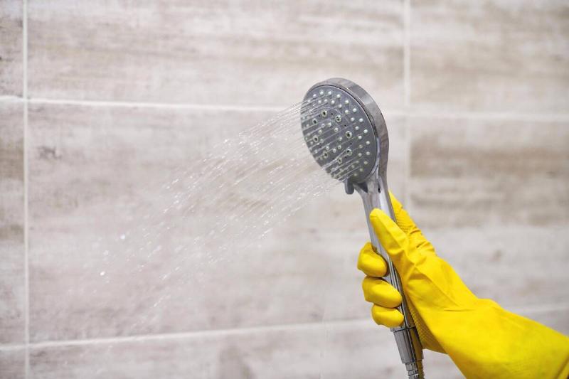 Hand in yellow glove holding shower head. 