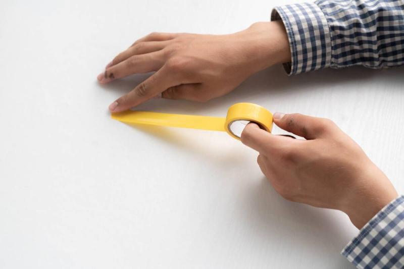 A person sticking yellow tape to a white surface. 