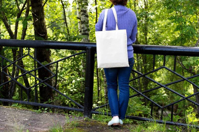A woman holding a tote bag and looking at trees. 
