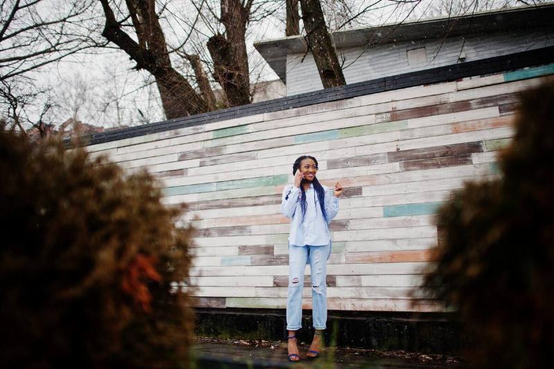 A woman standing in front of a reclaimed wood panel fence. 