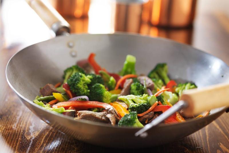 A steel wok with vegetables inside of it. 