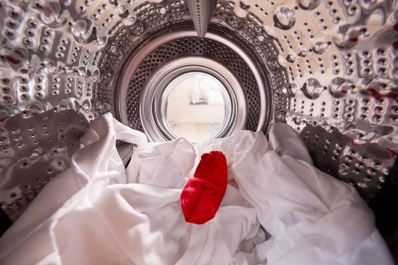 A re sock in white clothes in a washing machine. 