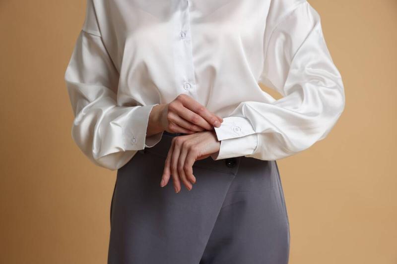 A woman adjusting the sleeve of a silk blouse. 