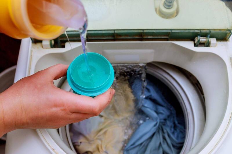 Hand pouring washing detergent in washer. 