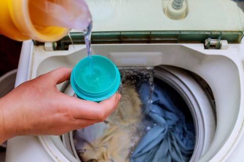 Hand pouring washing detergent in washer. 