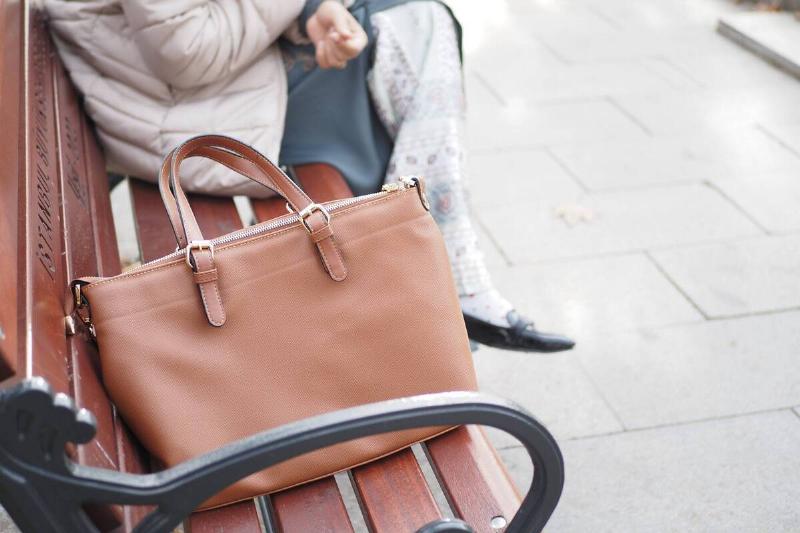 A woman sitting with her purse on a park bench beside her. 