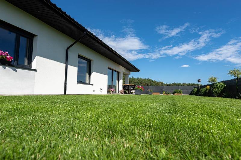 Beautiful garden with green grass, visible terrace table and house in beautiful summer weather, very wide shot.