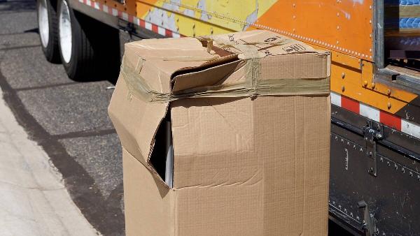 A cardboard box that has been damaged with the corner ripped open. 