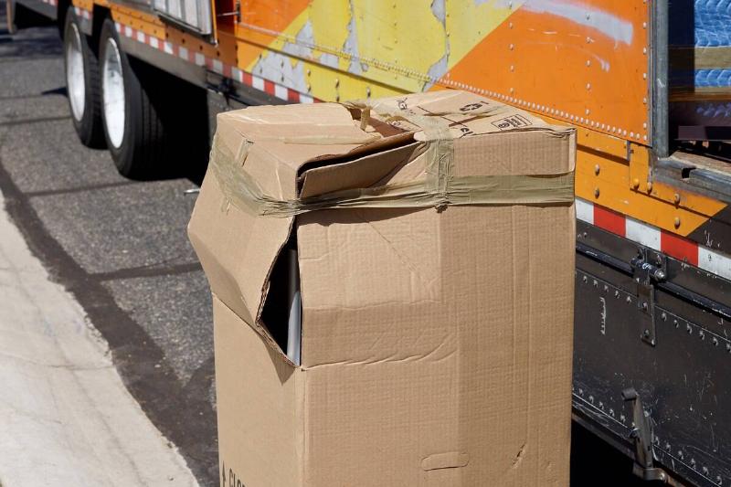 A cardboard box that has been damaged with the corner ripped open. 