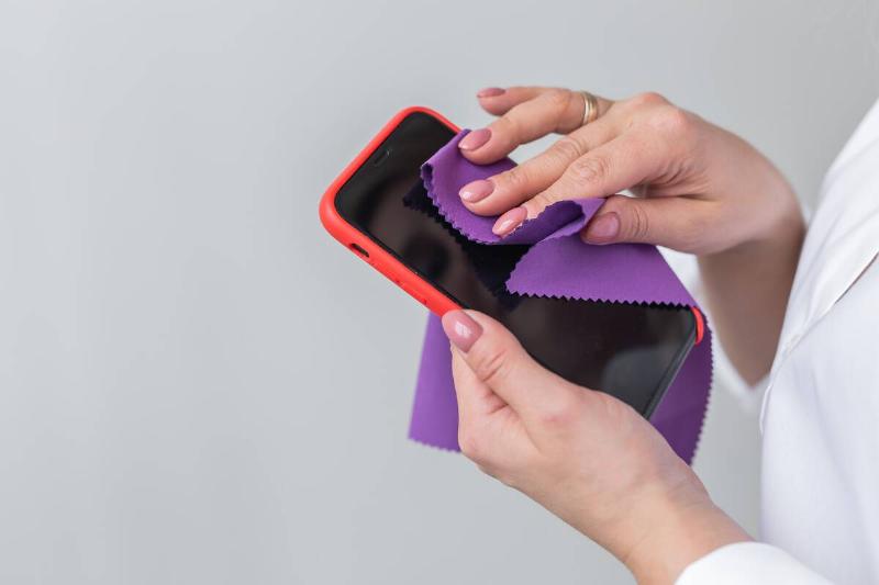 A woman wiping a microfiber cloth on a phone screen. 