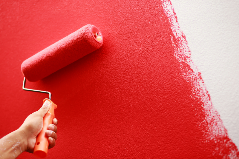 Paint roller putting red paint on a wall.