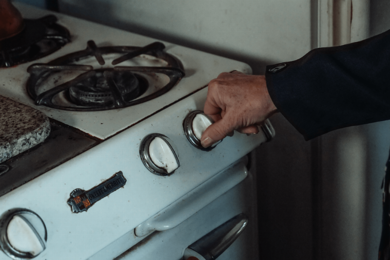 Hands adjusting the knobs on a stove.