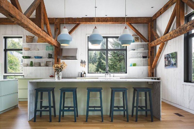Beautiful farmhouse style kitchen with floating white shelves, light green cabinets, and blue island stools.